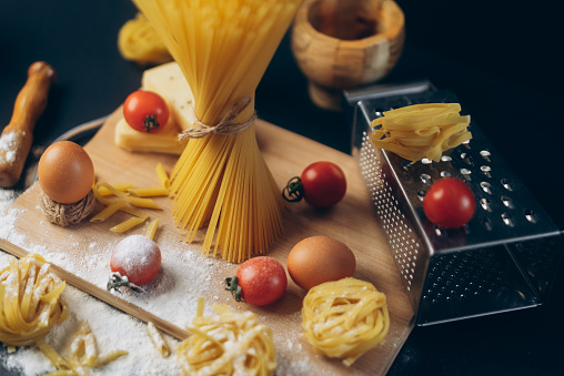 Pasta, tomatoes, and eggs lying on a table on dark background and preparing for being cooked with olive oil.