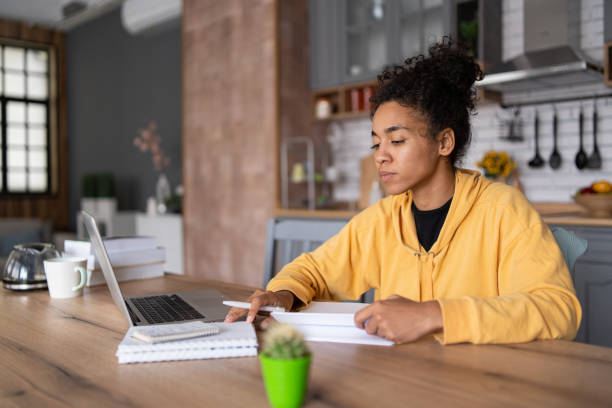 istock An african-american young woman is using laptop computer for remote work or studying online, she takes notes watching webinars or classes at kitchen table at home 1453620994