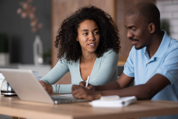 istock Modern young African American couple watching online learning classes, sitting in the kitchen, taking    notes and discussing, e-learning concept 1453621006