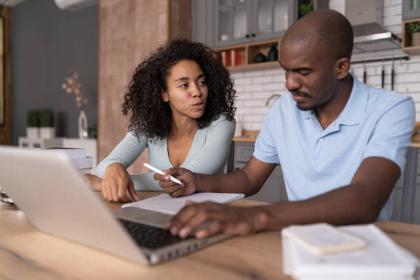 istock Modern young African American couple watching online learning classes, sitting in the kitchen, taking    notes and discussing, e-learning concept 1453621023