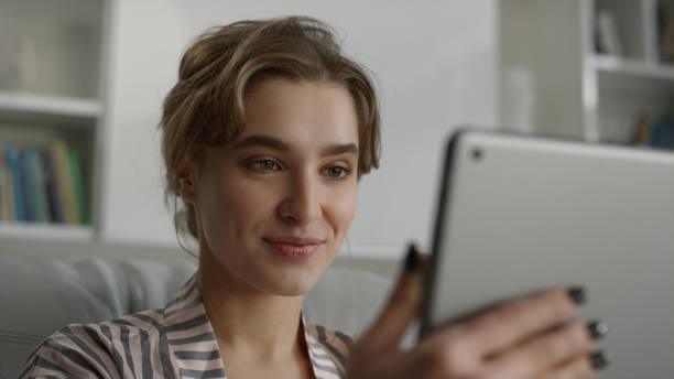 istock Girl finishing video call talking on sofa closeup. Cute blonde using tablet. 1453621068