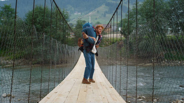 istock Backpackers standing river bridge on mountains hike. Happy couple play around. 1453623039