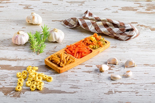 A closeup of different kinds of Italian pasta, macaroni presented on a wooden board beside some garlic