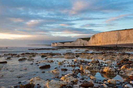 Sunset at low tide at the Seven Sisters Chalk Cliffs, Birling Gap, near Eastbourne, East Sussex, UK.  The evening sky is dramatic and reflected in the sea and the rock pools. The shingle beach is visible in the background under the rolling chalk cliffs.