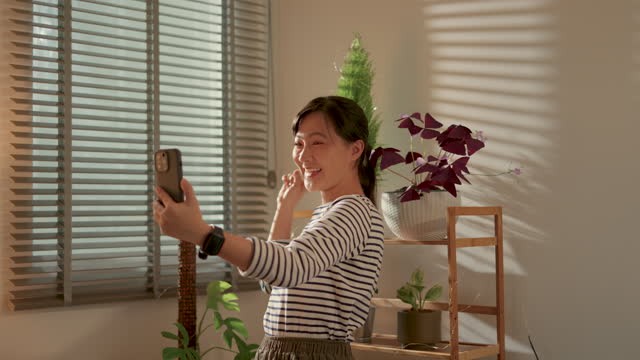 Asian woman using smart phone for video call or live streaming in living room at home.