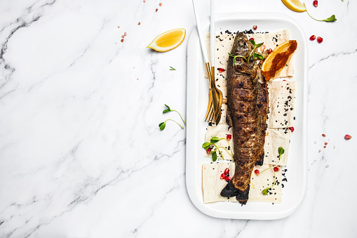 Baked trout fish with salt, lemon. Grilled trout. Fish dish fried fish fillet with vegetables on a light background. Ketogenic, keto or paleo diet lunch, Healthy food trend. Top view.