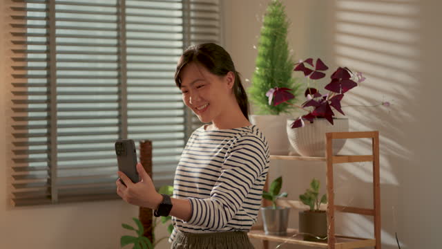 Asian woman using smart phone for video call or live streaming in living room at home.
