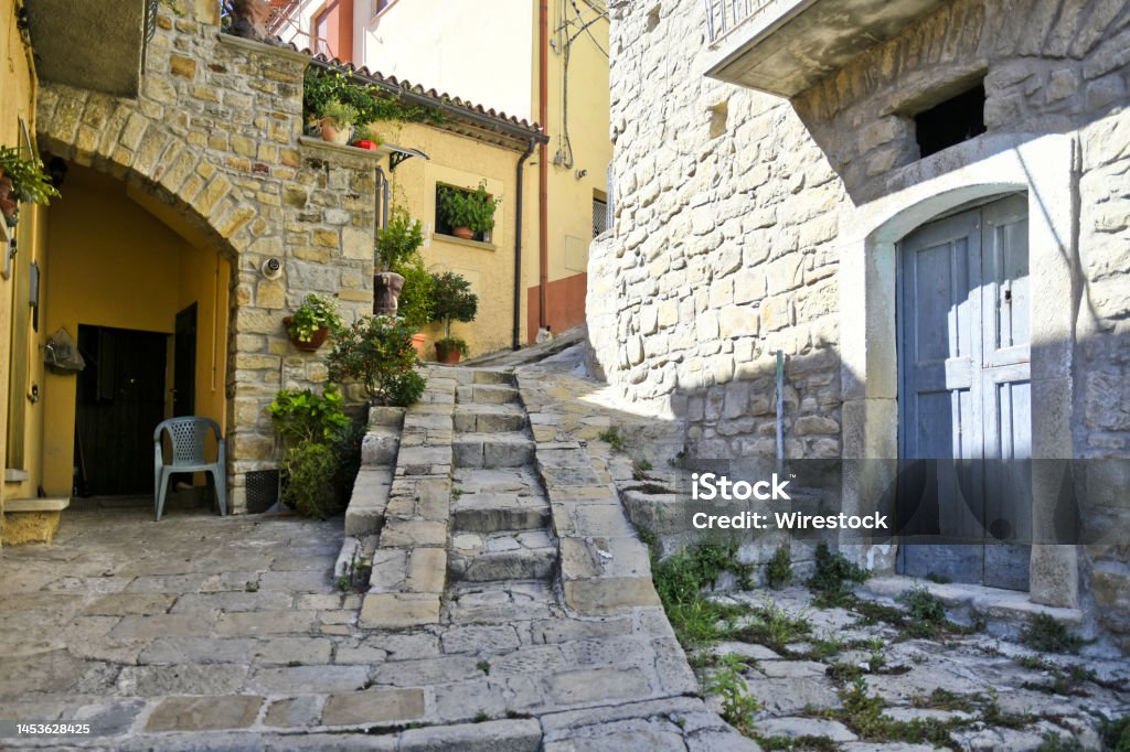 A narrow old street decorated with flowers, Stairs going up. Architecture of the old style. A narrow old street decorated with flowers, paved with stone. Stairs going up , Castelmezzano a village in the Basilicata region of Italy. Alley Stock Photo