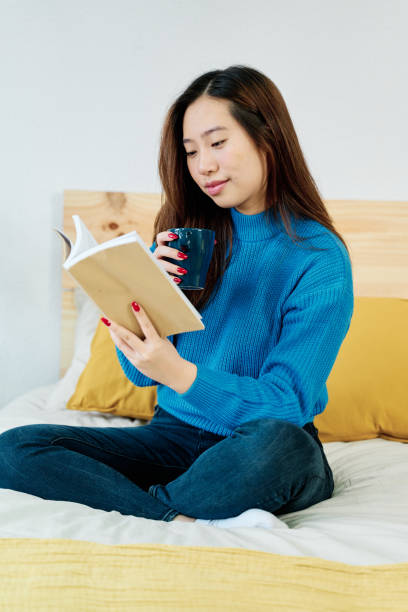 istock Young woman reading book in her bedroom 1453632258