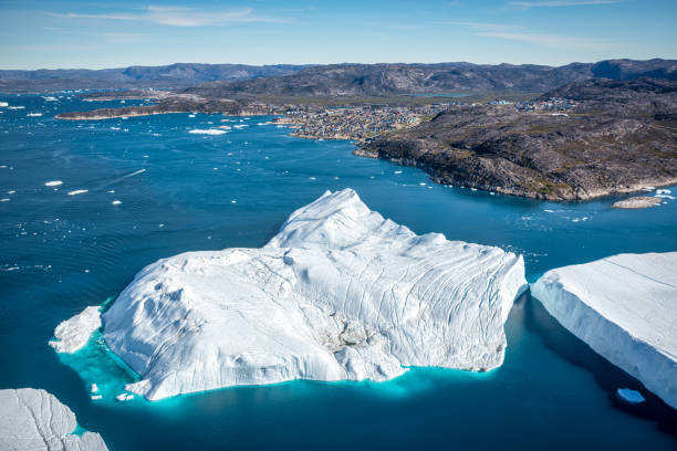 huge icebergs floating in front of Ilulissat, Greenland Aerial view of huge icebergs floating in front of colourful houses in Ilulissat, Greenland. Ilulissat lies 200 km north of the Arctic Circle in Qaasuitsup municipality, Western Greenland ilulissat icefjord stock pictures, royalty-free photos & images