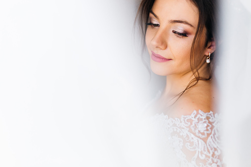 Close-up of the face of the bride with a beautiful make-up on the background of white curtains