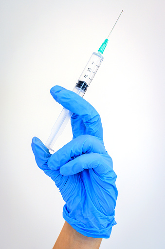 Close up photography of syringe in hand. Healthcare worker is wearing blue protective gloves.