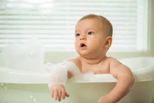 Photo of Cute little baby sitting in white bathtub
