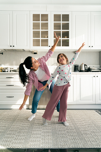 Happy young mom and little daughter dance at home
