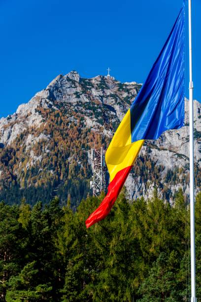 istock Romanian flag waving and wood trees under Bucegi mountains and blue sky, vertical shot 1453641025