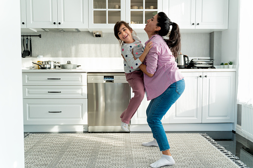 Cute girl feels great dancing with her mom in the kitchen