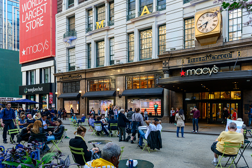 New York City, USA - May 20, 2014: Large group of people with Macy's Herald Square Store which is the flagship store for Macy's located on Herald Square in Manhattan, New York City. Pedestrians in crosswalk at busy midtown Manhattan shopping district of Herald Square and Large group of people sitting on the street