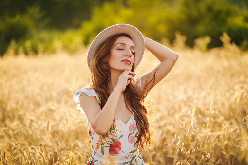 Happy young woman in wheat field by sunset