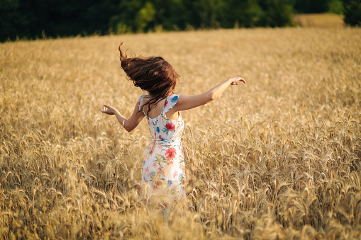 Happy young woman in wheat field by sunset