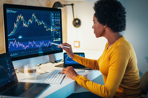Business woman checking stock market chart on digital devices. Trading app on device screens. Female Fund manager looking at stock market chart, using computer, laptop and digital tablet. Business woman making money as crypto trader investor broker at home. Woman at home office trading Online