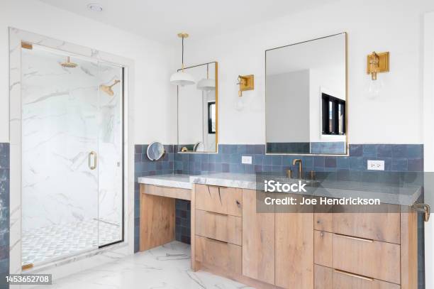 A Bathroom With A Wood Cabinet Gold Accents And A Marble Shower Stock Photo - Download Image Now