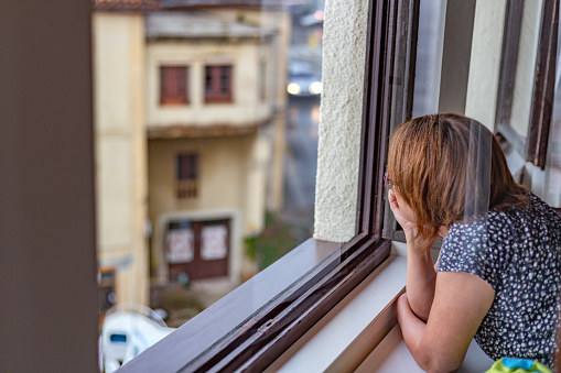 Lastres, Asturias, Spain. August 8, 2022. Overhead view of middle-aged woman looking away through open window in rural setting at sunset