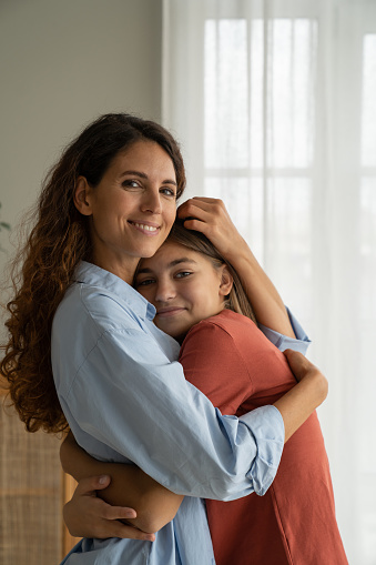Portrait of happy mother and teenage girl daughter cuddling hugging and smiling at camera, spending time at home, mom and adolescent kid having healthy, supportive relationships. Happy teen parenting