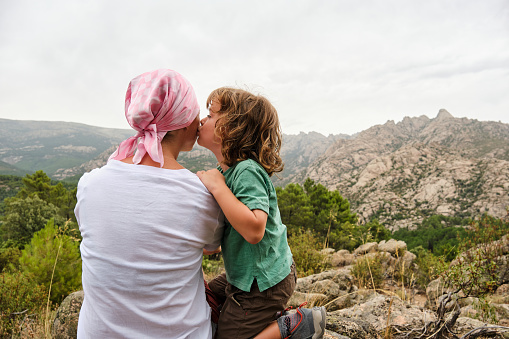 Woman with cancer relaxing in nature. She is with her son who is giving her a kiss.