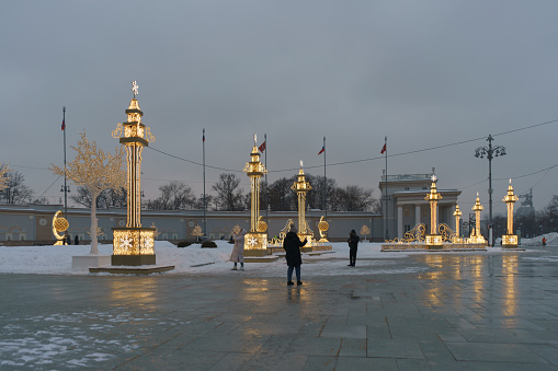 Moscow, Russia - December 30, 2022: Bright golden decoration of the entrance of the Exhibition of Achievements of National Economy (VDNkH) in Christmas. People walk and make photographies