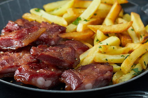 Grilled tasty ribs with French fries in an iron pan, with barbecue sauce on a dark wooden rustic background