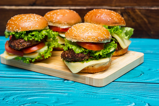 Homemade hamburgers with meat, cheese, lettuce, tomato on a wooden table, served on cutting board