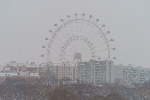 The ferris wheel during winter blizzard with grey sky as background. Residential district. Wonderful view. The Sun of the city Moscow view