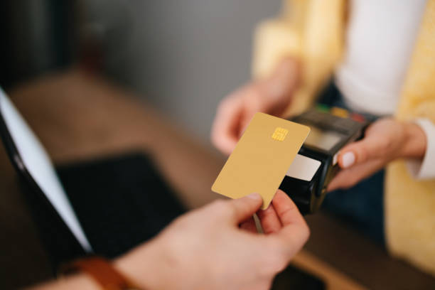 Close Up Photo Of Woman Hands Paying With Credit Card In A Home Decor Store From above photo of an anonymous woman holding credit card reader while African-American customer paying bill using contactless payment. paying stock pictures, royalty-free photos & images