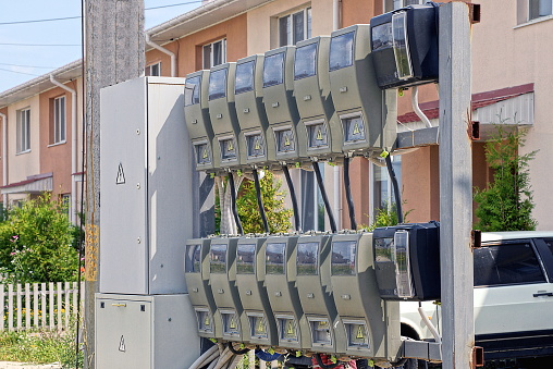 a row of gray electric meters and a metal box for electrical wiring on the street against the background of a private house