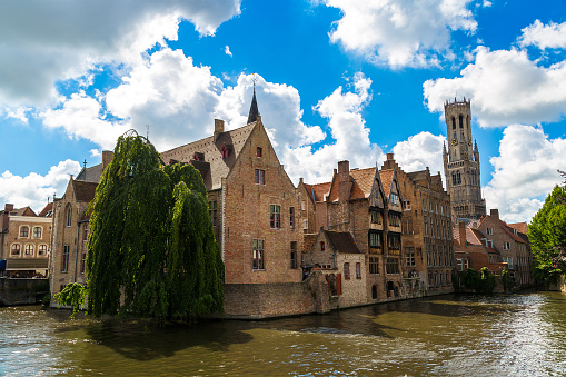 Canal in Bruges and famous Belfry tower on the background in a beautiful summer day, Belgium