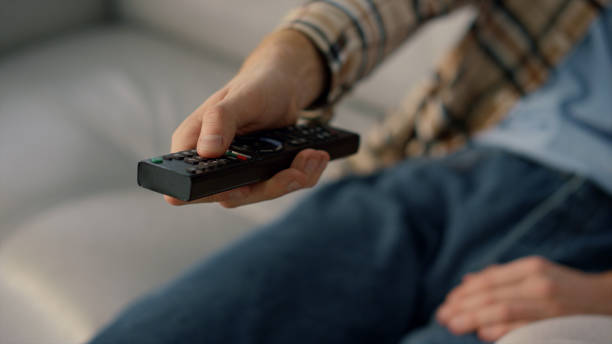 istock Closeup hand zapping tv resting at home. Man watching television on sofa alone 1453676286