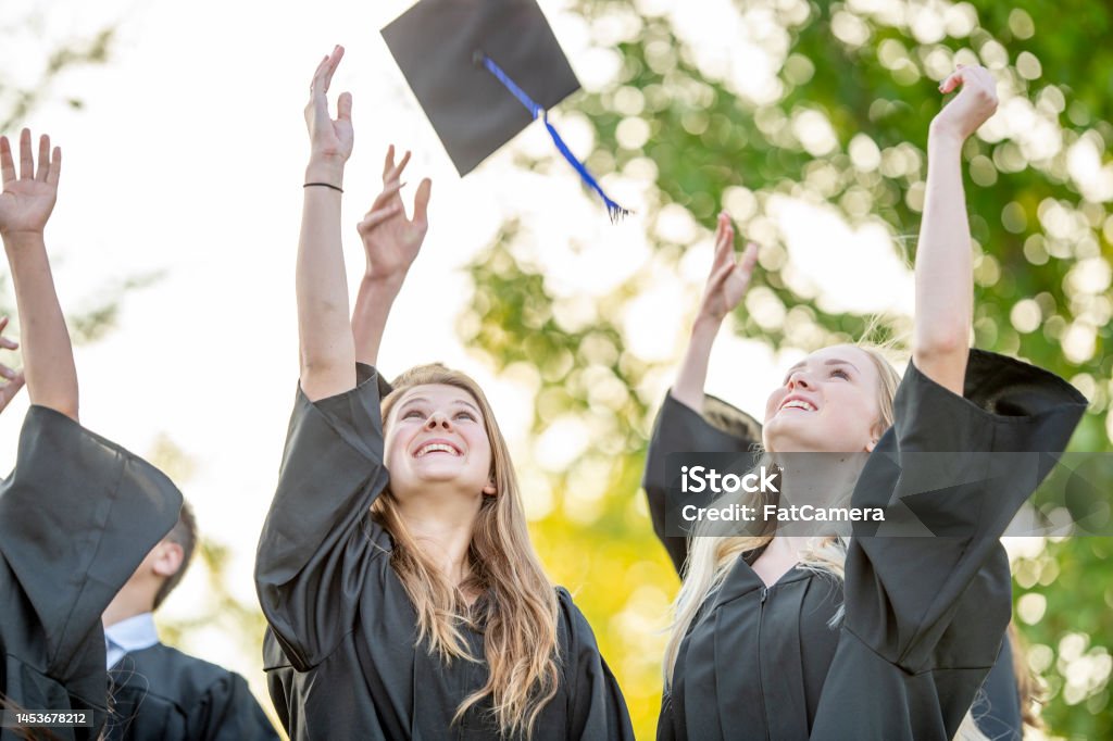 Celebrating Graduation A small group of graduates toss their caps into the air as they celebrate their achievements together.  They are each wearing a gown and are smiling with joy as they cheer and celebrate. 14-15 Years Stock Photo
