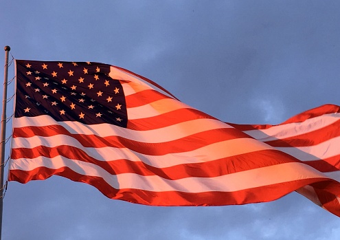 American Flag at sunset with blue / dark grey sky waving (wind)
