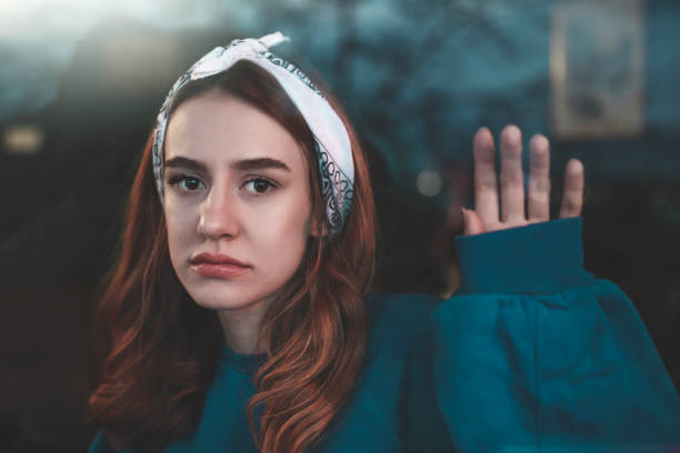 Portrait of a depressed woman: pale face, downcast eyes, expression of sadness and fatigue, shadows under the eyes, disheveled hair, blurred and dark background.