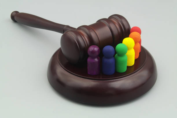 People figures colored in rainbow colors with wooden judge gavel on gray background. stock photo