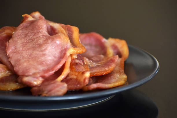 Back bacon on a blue plate. Back bacon on a blue plate. Selective focus. cooked bacon slice stock pictures, royalty-free photos & images