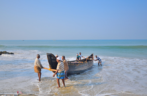 Varkala, India - March 05, 2018: A group of fisherman pulling a boat from the sea.