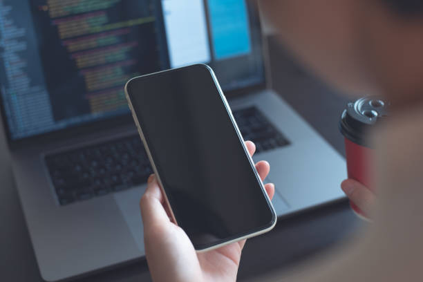 istock Mockup image, woman holding mobile phone with blank screen template during working on laptop 1453722607