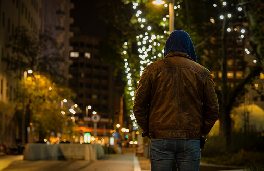 Rear view of adult man on street at night with lights of Christmas