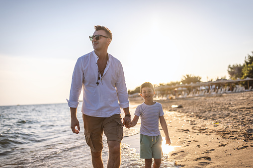 Photo of dad and son holding hands while walking on the beach