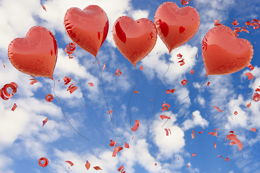 Red heart shaped balloon flying in a blue sky background