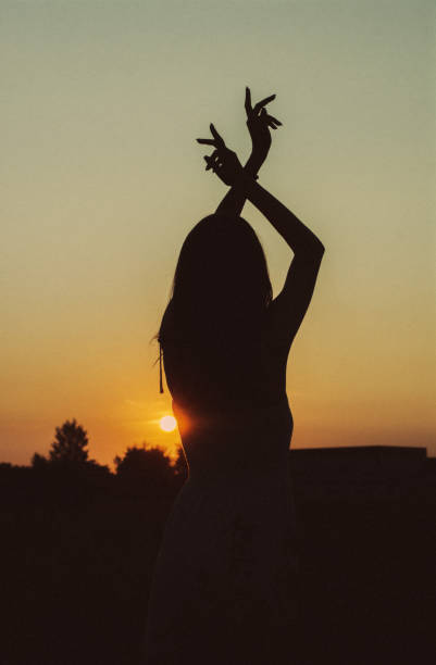 istock Vertical silhouette of a female posing with her hands up during sunset 1453725874