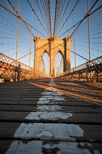 A vertical shot of the Brooklyn bridge in the early morning with sunshine on it in New York
