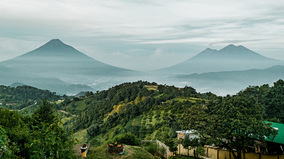 A beautiful landscape view of green plants on hills and Volcan de Fuego mountains on the horizon in Antigua, Guatemala