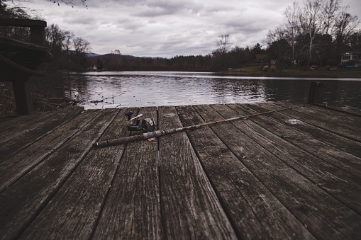 An old abandoned fishing rod rests on a wooden dock before the lake